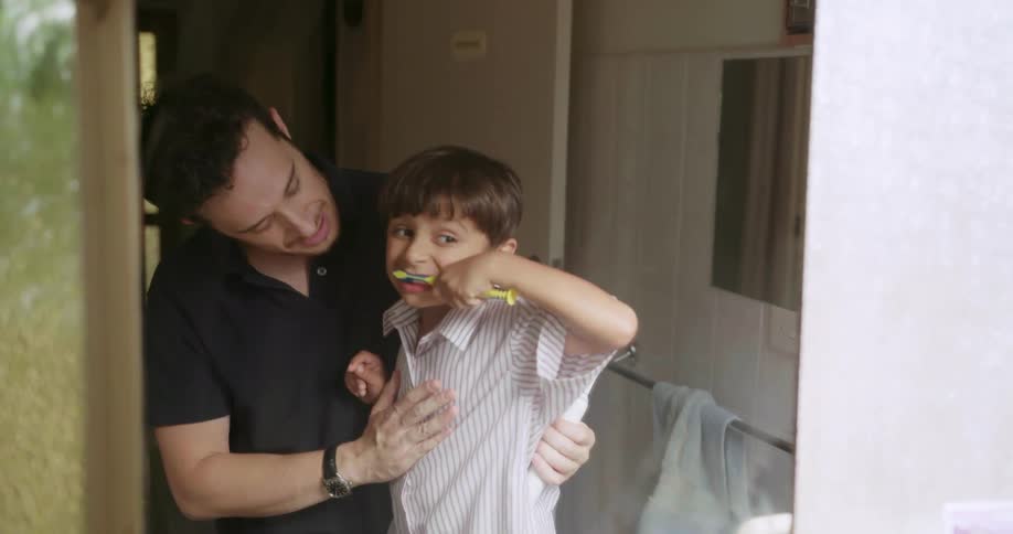 A man is teaching his son how to brush his teeth