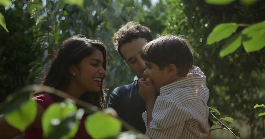 A child tries a fruit picked from a tree and shows his feelings about it to his parents as they stand in an orchard
