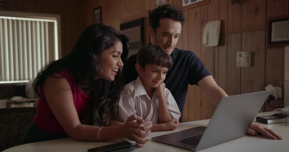 A young family is gathered around a laptop