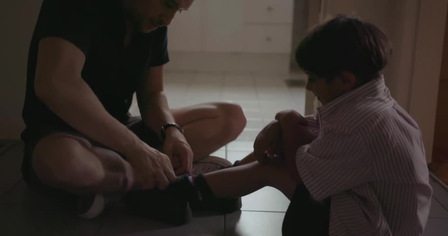 A man ties the shoes of his child in the hallway