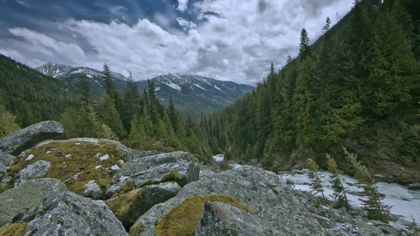 Clouds move over a forest and mountain peaks