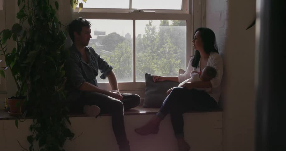 A couple and their baby sit on a window sill