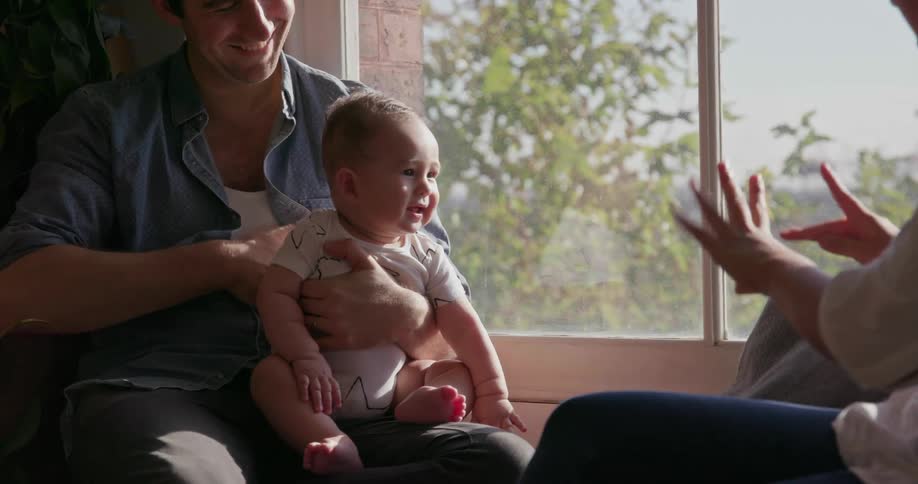 Man holds baby on lap while woman makes baby laugh