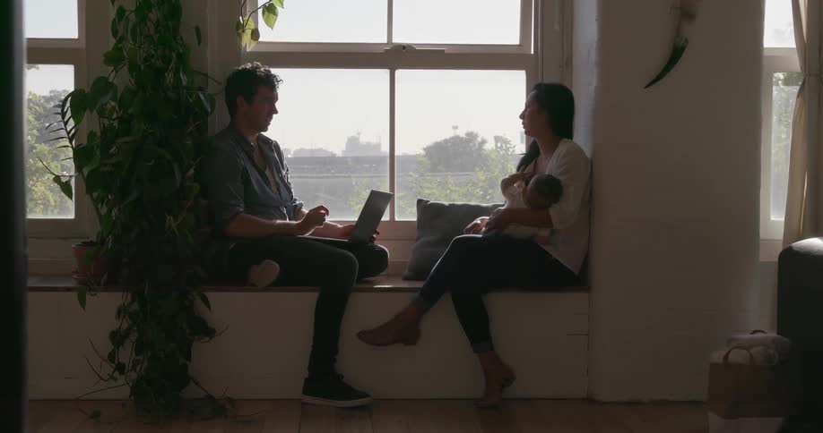 A man and woman talk while sitting on a window seat with a baby