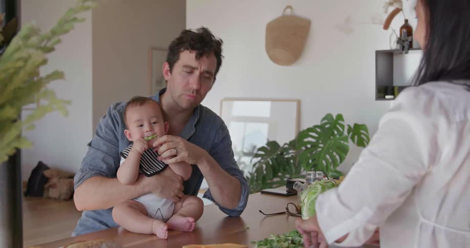 A man is holding his baby as he talks with his wife in their home in daylight