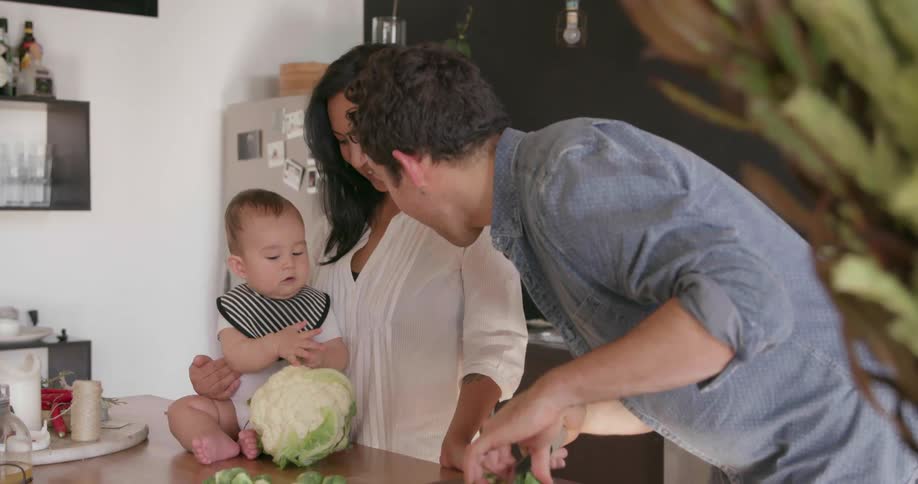 A man cuts vegetables while talking to a baby