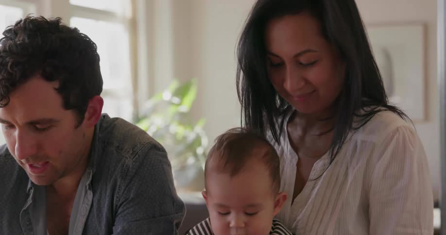 Woman plays with a baby as a man works on a laptop