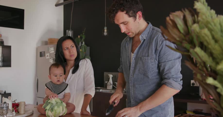 Man slices food as a woman and baby watch