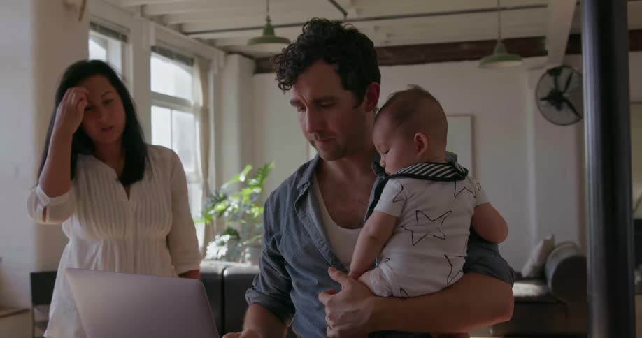 A man holds a baby while typing on a laptop