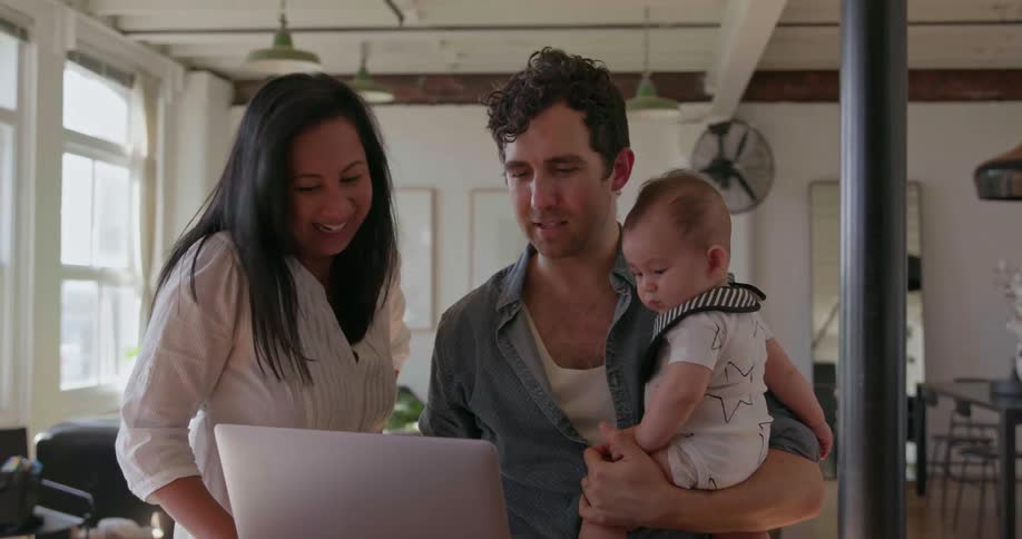 A family are holding a baby and using a laptop