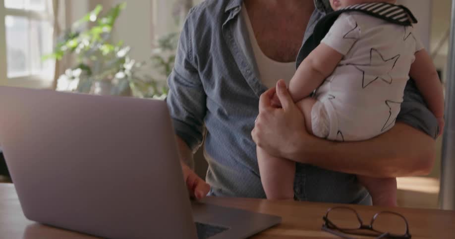 A man holds a baby by the laptop
