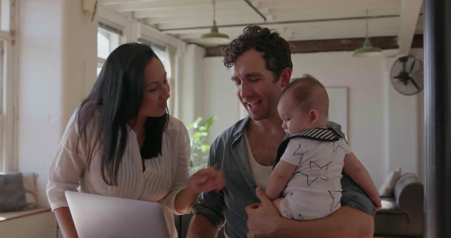 A man holding a baby talks with a woman as they look at a laptop