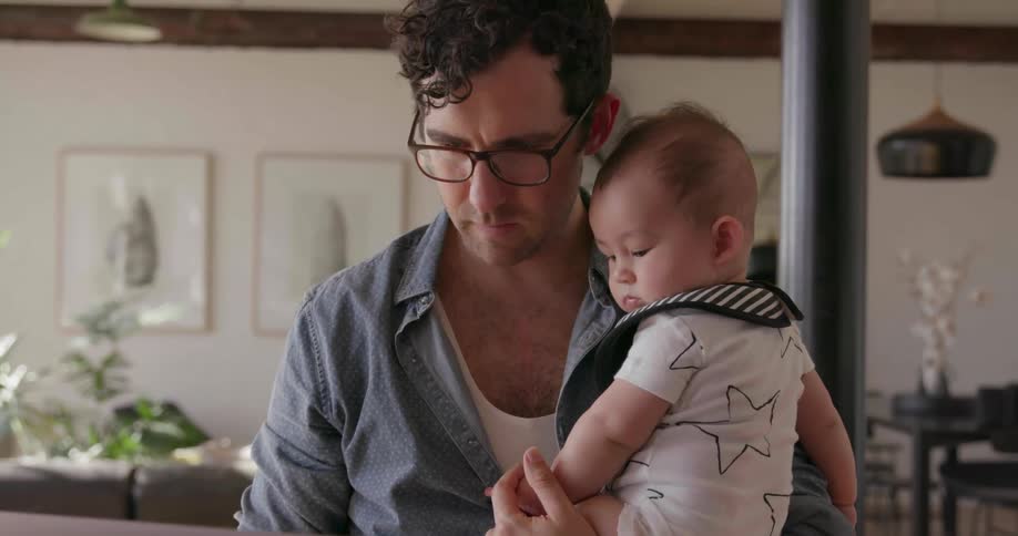 Man holds baby while typing on laptop