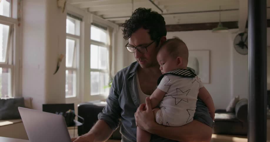 A man holds a baby as he uses a laptop