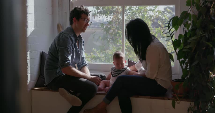 A couple and baby sit on a window sill