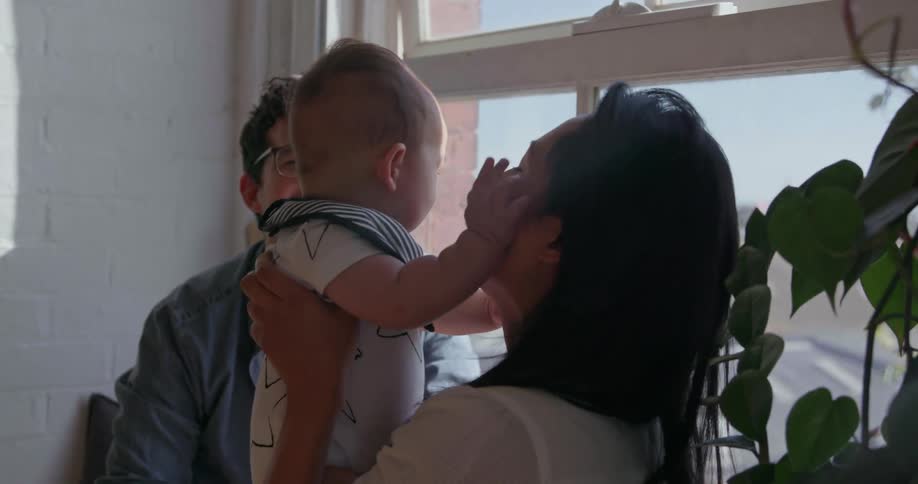 A baby is patting its mother's face as they sit in a window in daylight