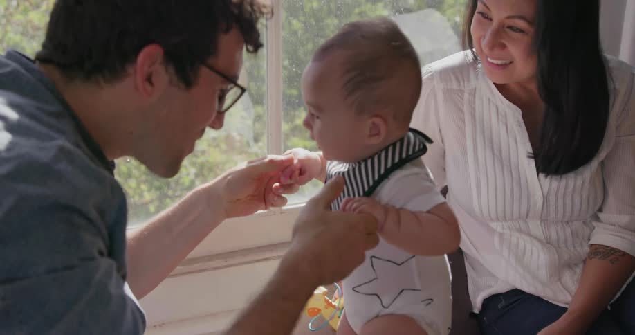 A father plays with his newborn son on a window bench