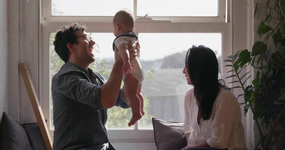 A couple are holding their baby as they sit next to a window