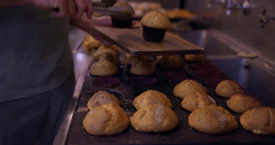 A man puts some muffins on a tray