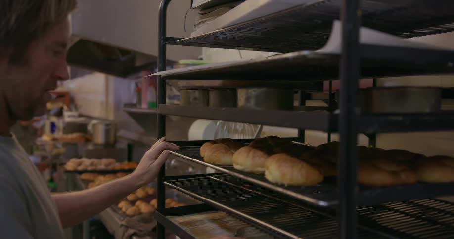 A baker puts a pan of baked goods on a rack to cool