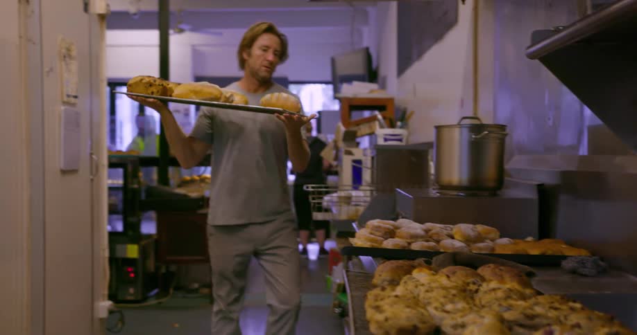 Man carries a tray of bread past trays of buns