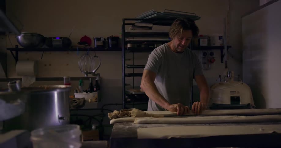 A man rolls out dough in a bakery