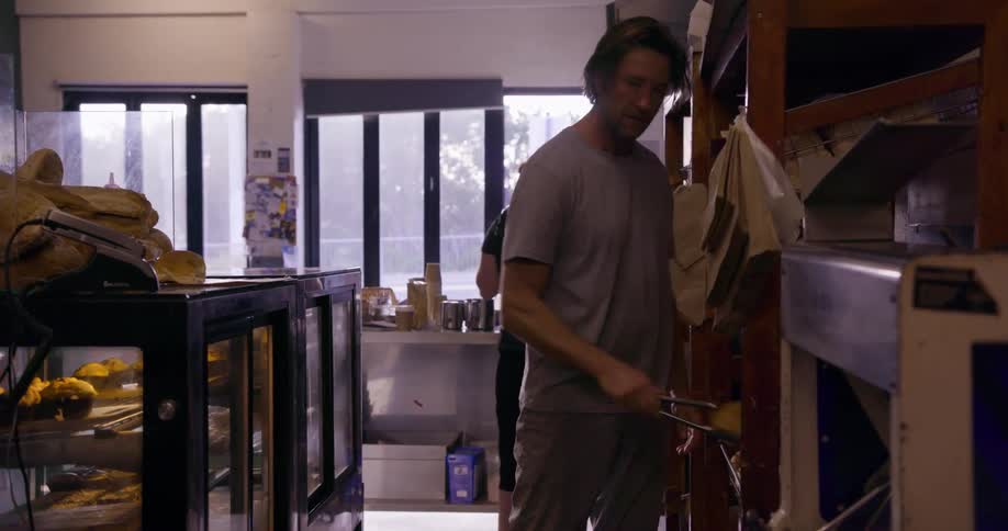 A man is pulling rolls off of a tray using tongs in a bakery