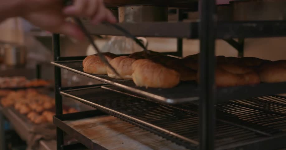 Man uses tongs to move buns from one tray to another