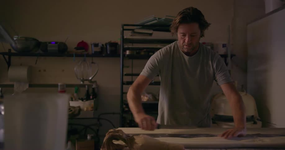 A man is placing dough on a table and cutting it