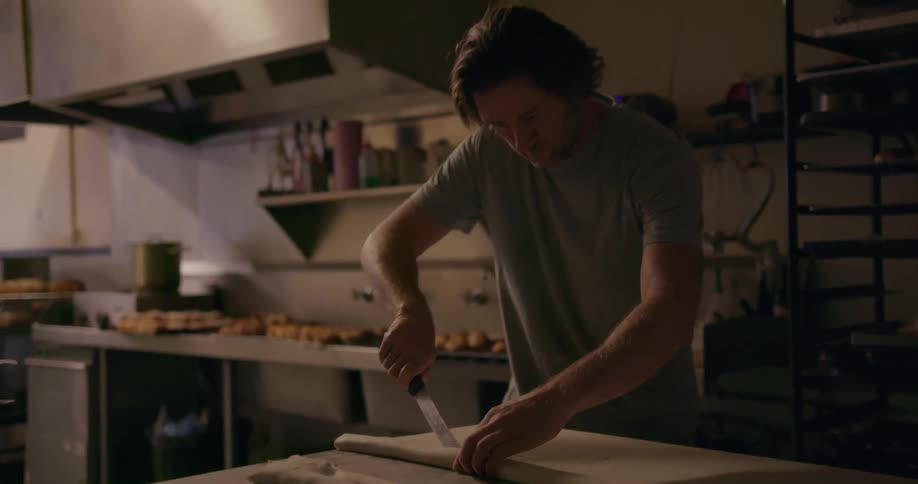 Man cuts large pieces of dough on a table