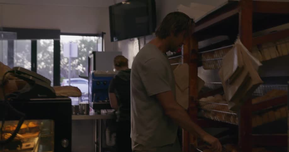 Man in a bakery uses tongs to place donuts in a wired shelf