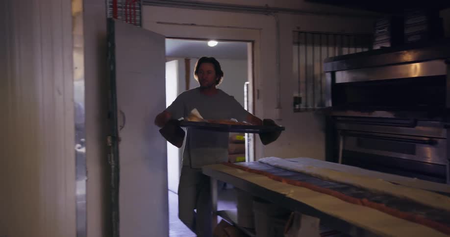Man takes food out of a large oven and puts in on a rack to cool