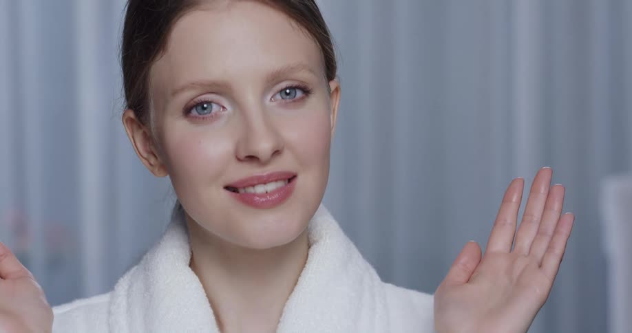 A woman touches her cheeks and removes her hands to show off her clear skin