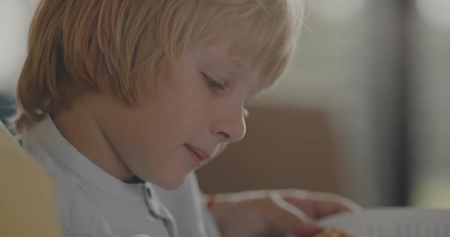 A boy is reading a book with his grandma and sitting indoors
