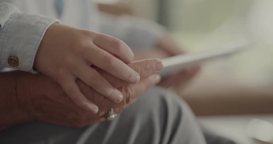 Child and elderly person hold hands and use tablet together