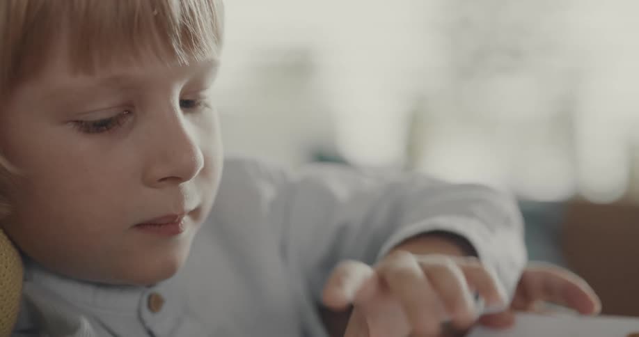 Boy sitting on the lap of one of his parents readnig a book at home