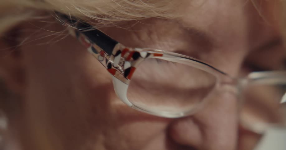 An elderly woman with blond hair and glasses is speaking to a child next to her