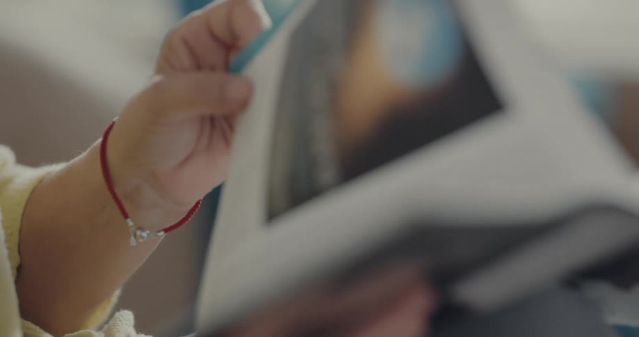 A person slowly flips through the pages of a magazine while sitting indoors