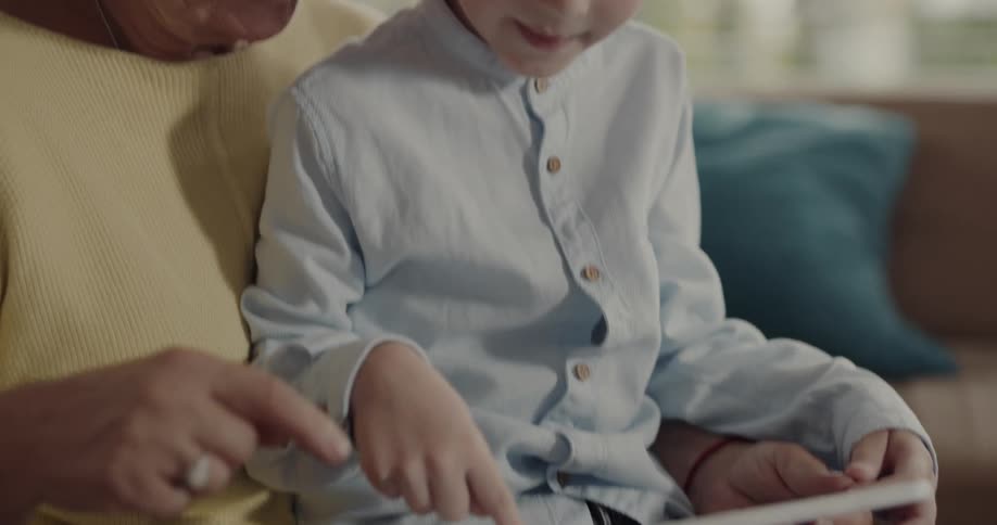 Grandmother and grandson playing on a tablet together on the couch