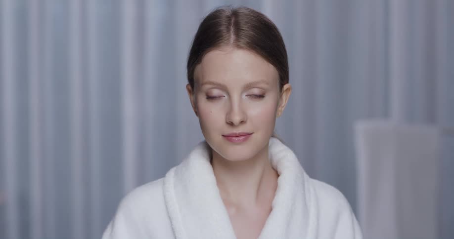 Woman wearing robe turns and stands with a light smile