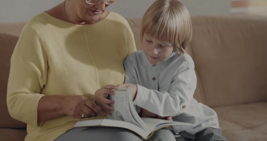 Grandmother is reading a book to her grandchild on the couch