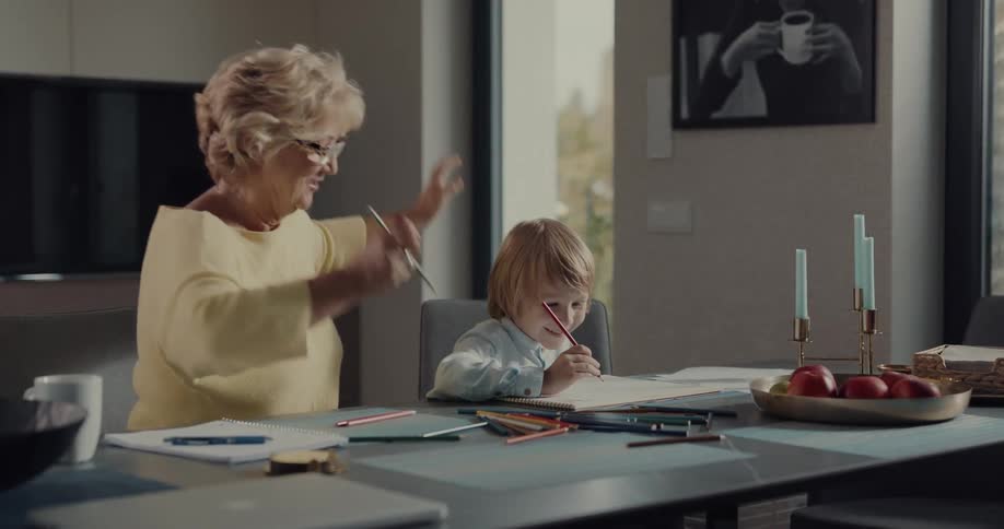 Grandmother draws with grandson as they sit at dining table