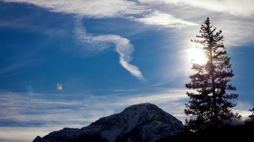 Clouds moving over a snowy mountain near a single tree