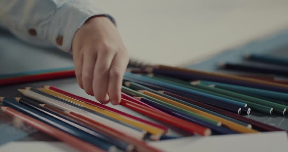A child is drawing on paper with colored pencils