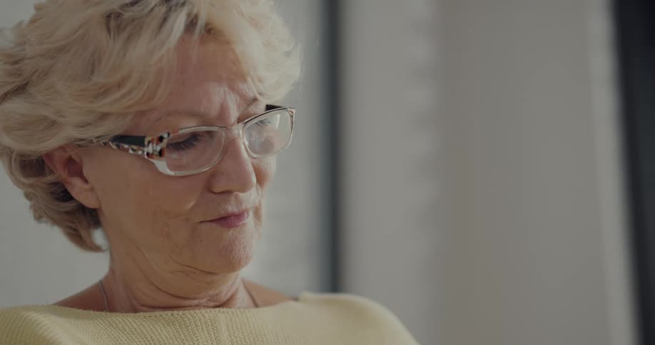 An elderly woman flips through the pages of a book while reading indoors
