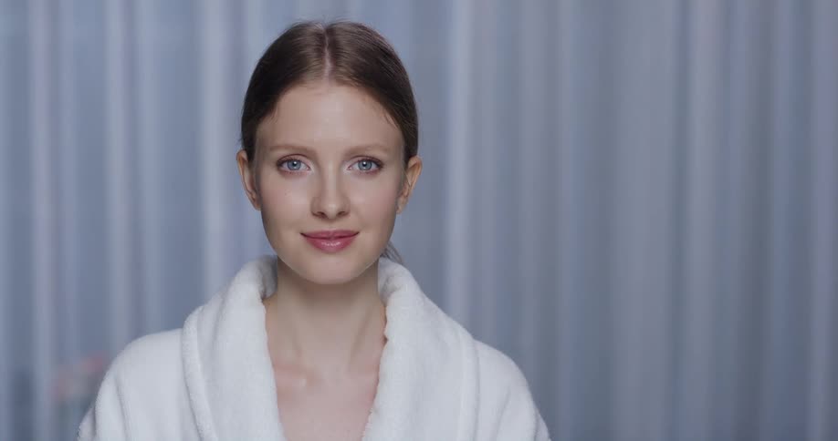 Female model with white bathrobe smiles slightly at camera in the studio