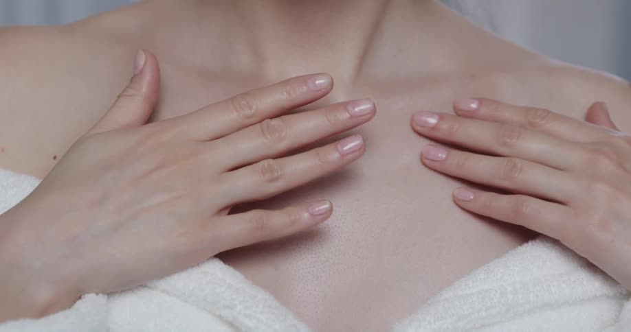 Woman wearing a white towel rubs cream over her chest