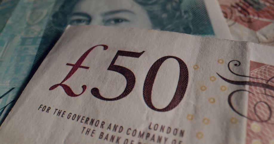 The value number on a british banknote lying atop a pile of money