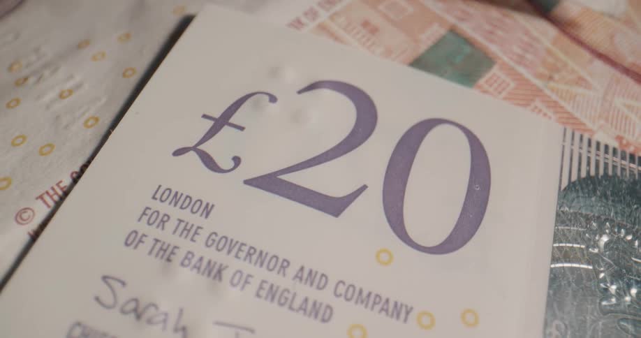 The value label on a british banknote lying atop a pile of currency