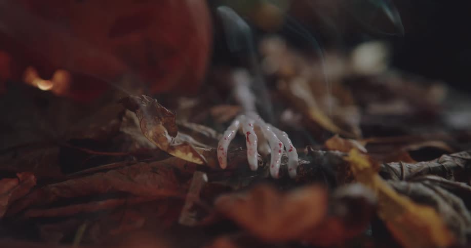 Close up of a toy skeleton hand over smoking dry leaves next to a pumpkin